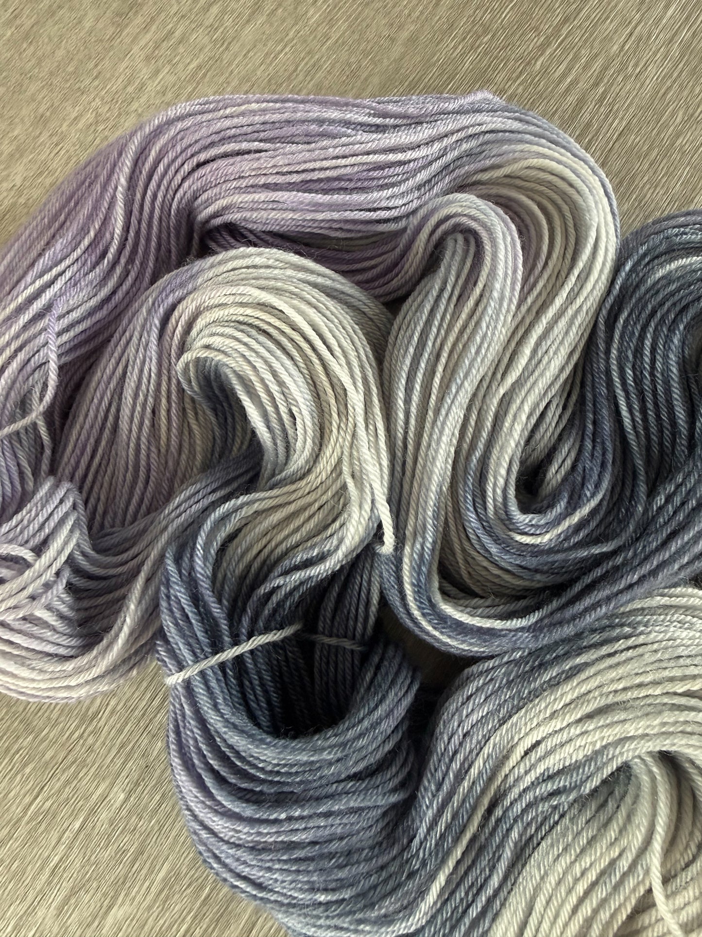 Hand-dyed ethically sourced merino wool yarn in deep blue, soft lilac, and muted gray, evoking twilight.