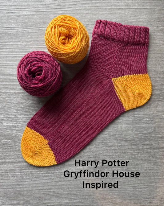 Knitted sock with Gryffindor colors and matching yarn on a gray background