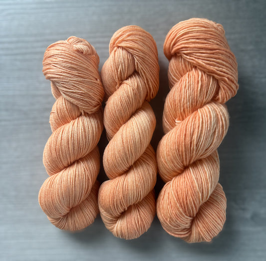 Three skeins of "Melon Dollar Smile" ethically sourced merino wool yarn in a semi-solid coral-peach hue.