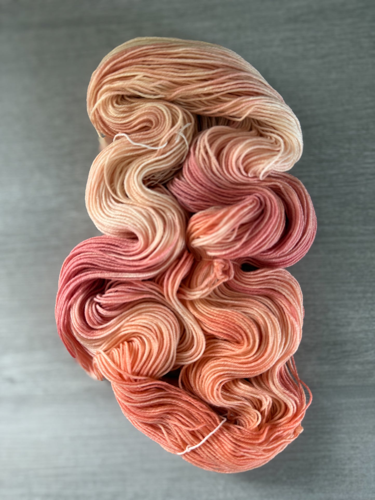 Ethically sourced merino wool yarn, hand-dyed in soft peach, ivory, and rose, creating a watercolor effect.