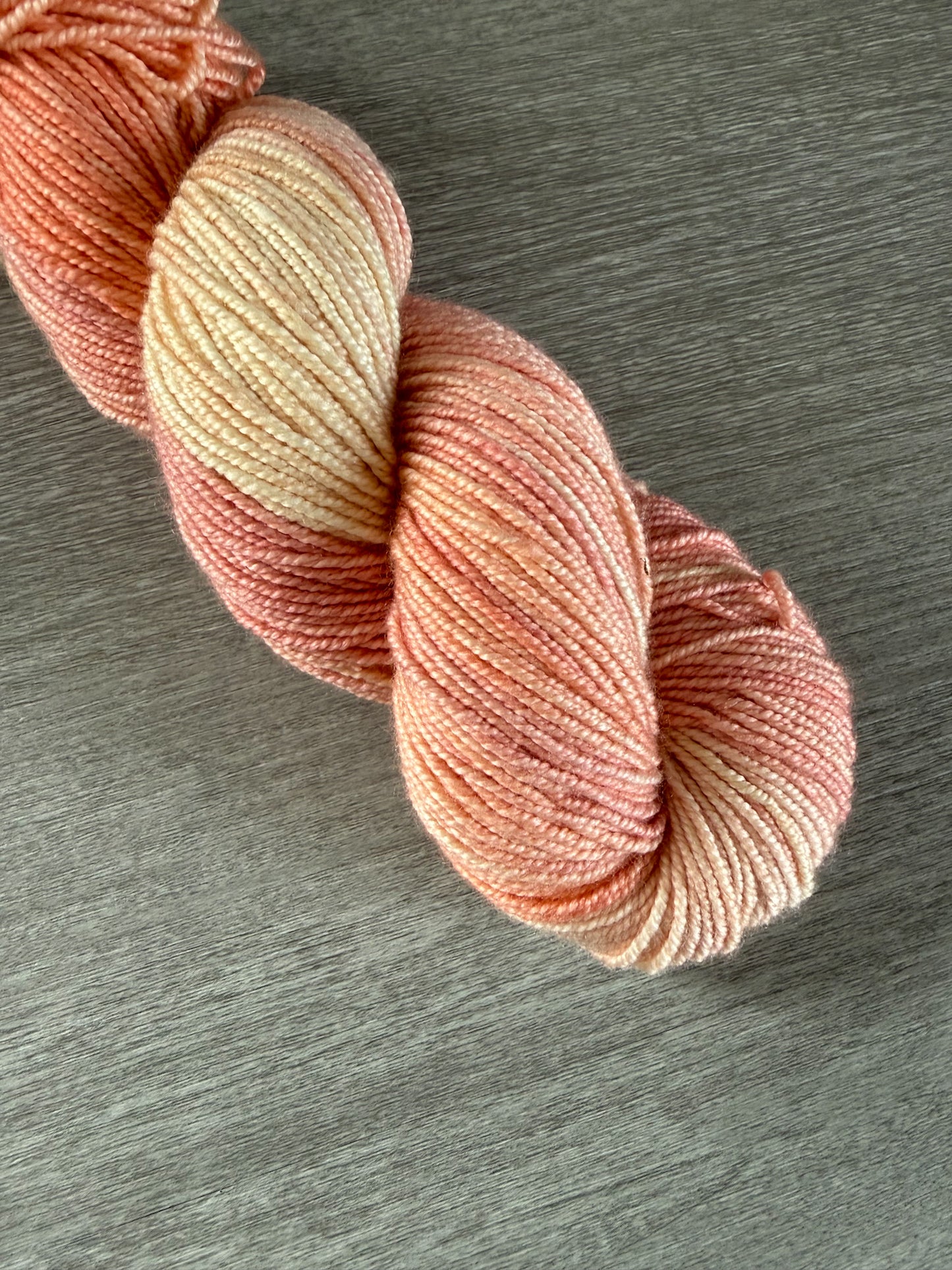 Hand-dyed Whispering Petals merino wool yarn in soft peach, ivory, and light rose hues.