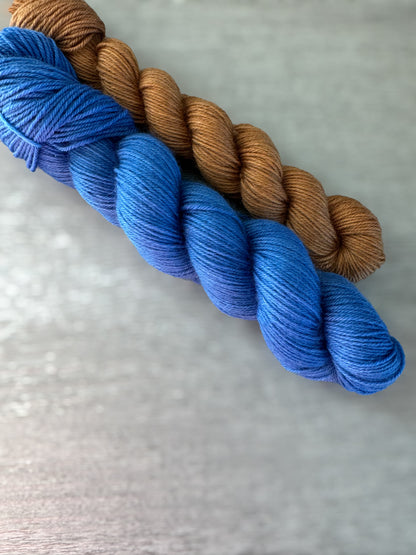 Two skeins of yarn, one blue and one brown, on a textured white background.