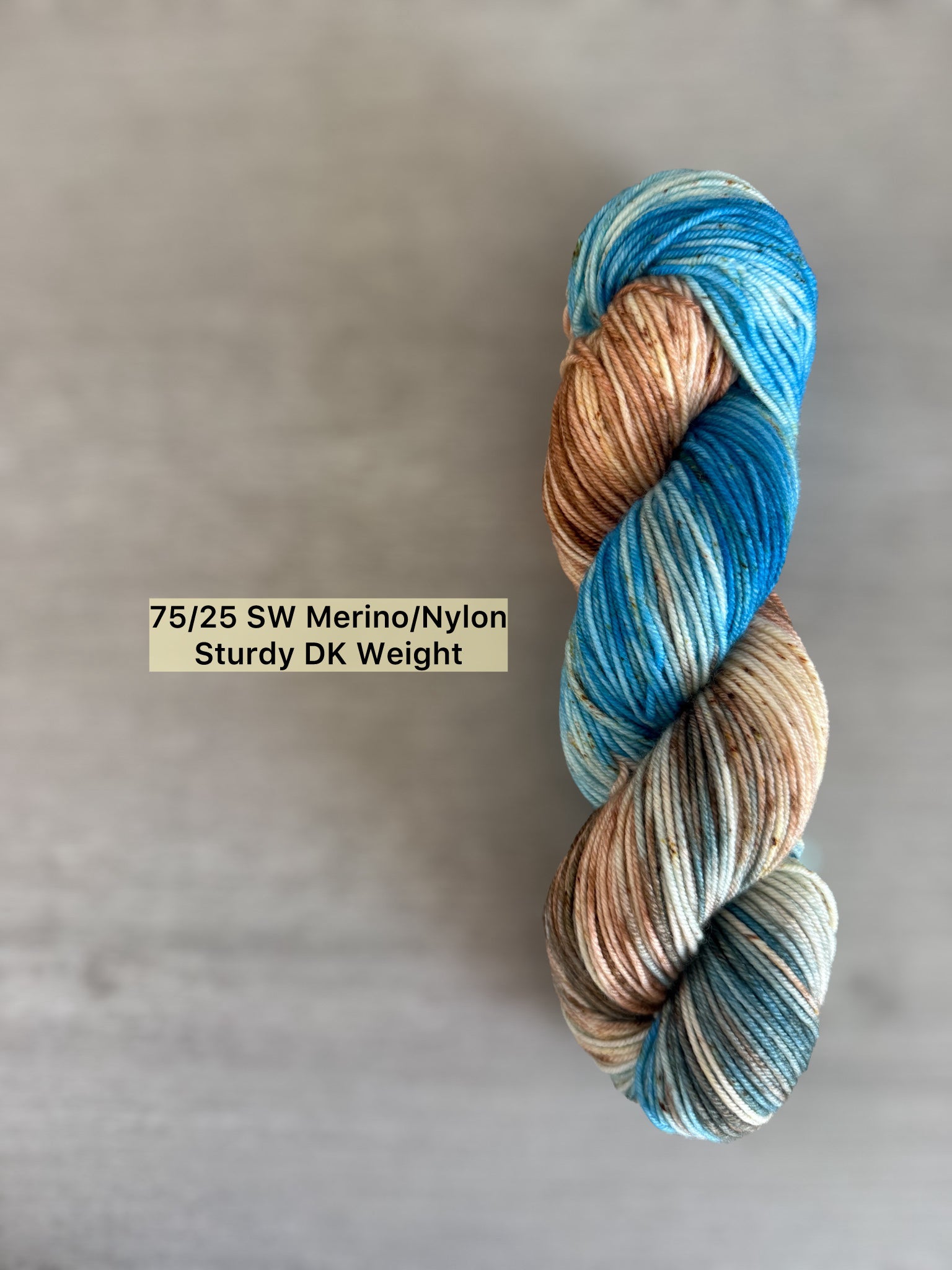 Hand-dyed ethically sourced merino wool yarn in variegated robin's egg blue, caramel, and brown speckles.