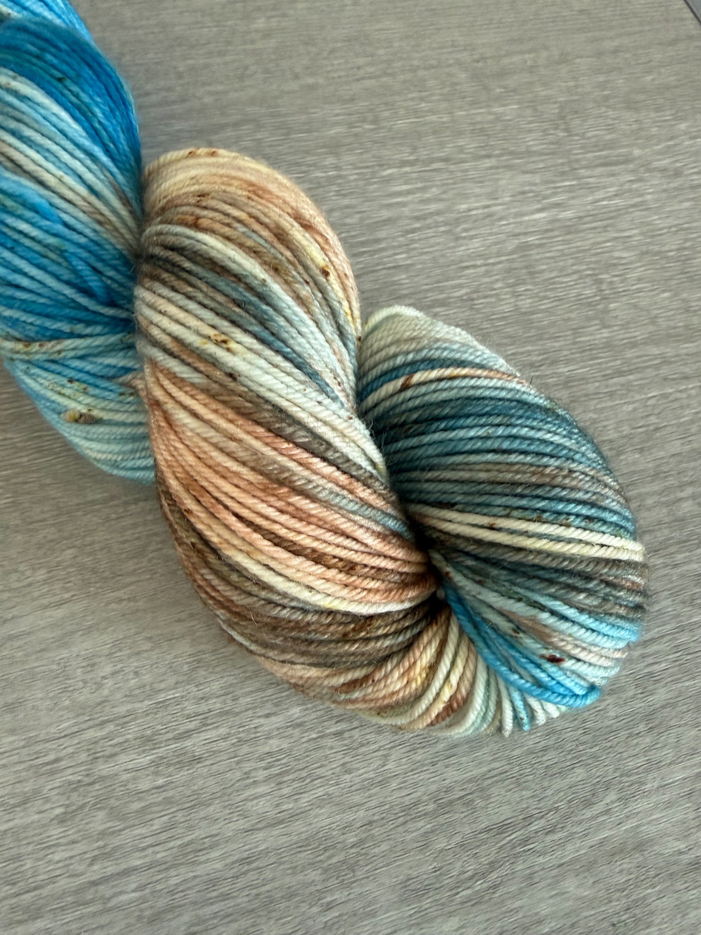 Hand-dyed variegated merino wool yarn in deep robin's egg blue, caramel, and brown speckles, ethically sourced.