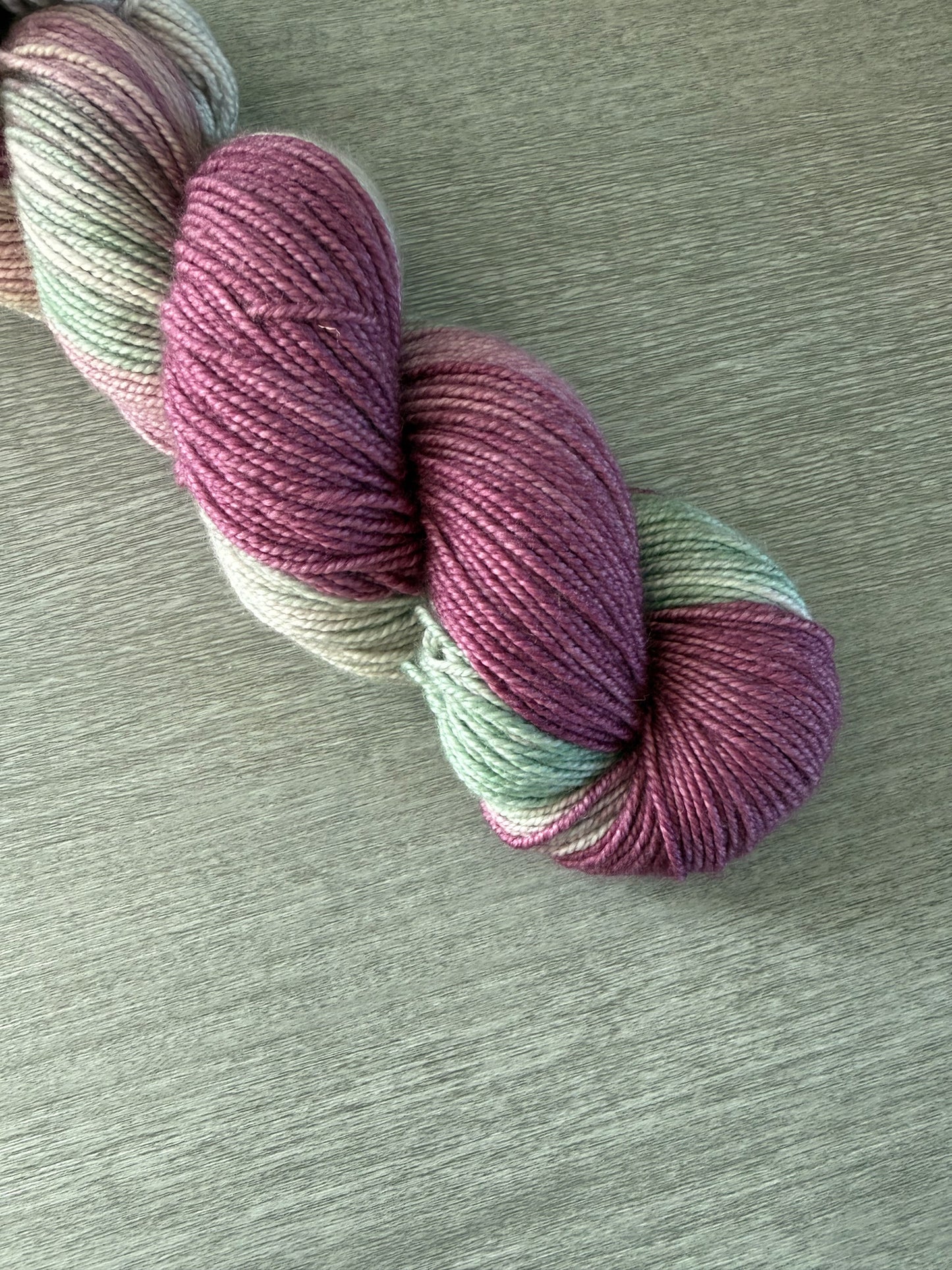 Ethically sourced merino wool yarn, hand-dyed in variegated plum, ivory, and sage green.