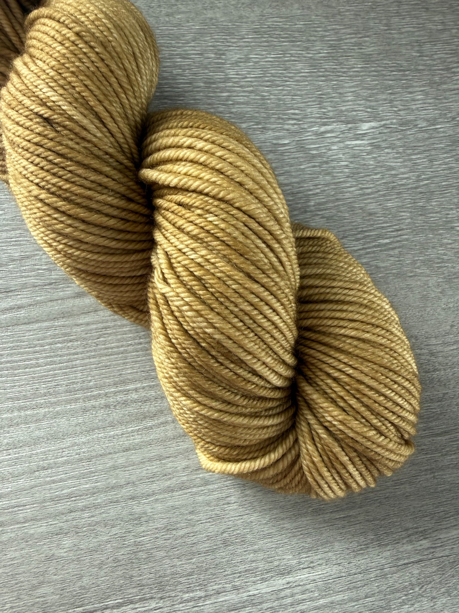 Hand-dyed "Adirondack Chair" golden merino wool yarn, ethically sourced, on a gray wood surface.