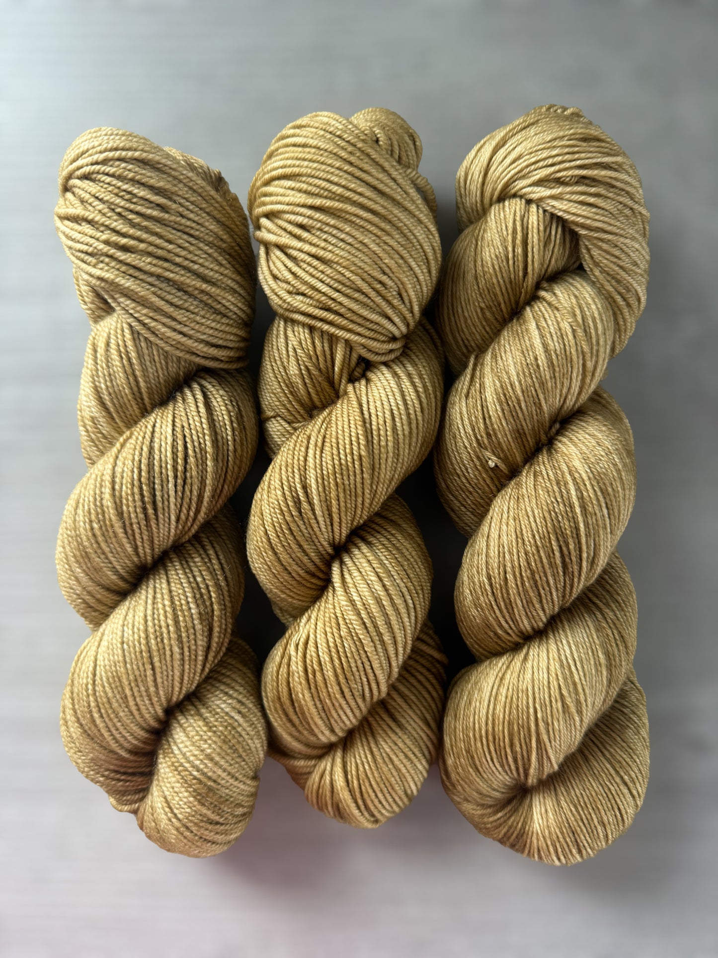 Three skeins of ethically sourced, hand-dyed golden merino wool yarn, "Adirondack Chair" colorway.