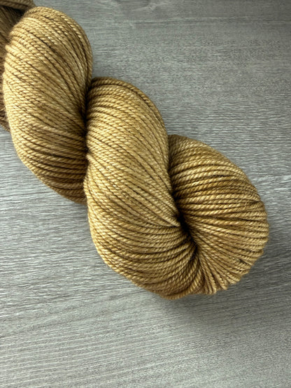 Skein of ethically sourced, hand-dyed "Adirondack Chair" golden merino wool yarn on a gray wood surface.