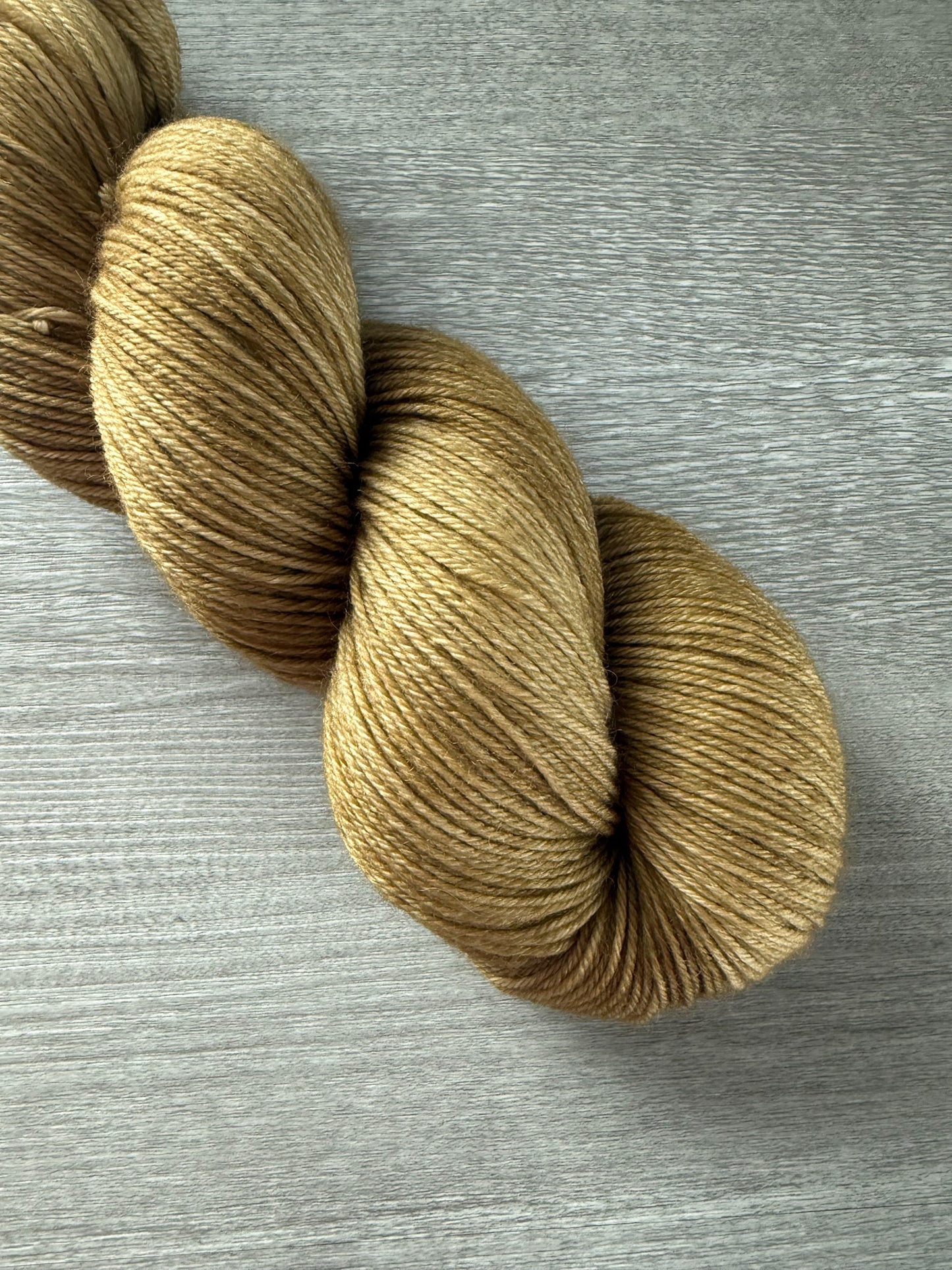 Ethically sourced "Adirondack Chair" golden-toned merino wool yarn skein on a gray wood surface.