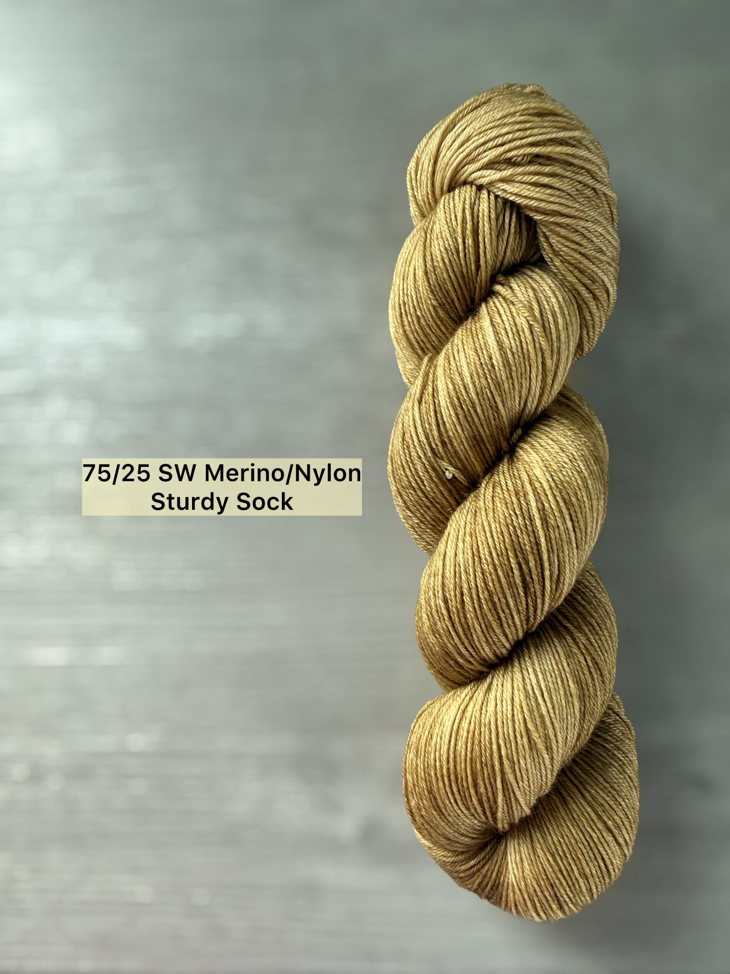 Hand-dyed "Adirondack Chair" golden merino wool yarn, ethically sourced, on a gray wood background.