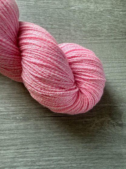 Bubble-gum pink artisan hand-dyed merino wool yarn skein, ethically sourced, on a gray wood surface.