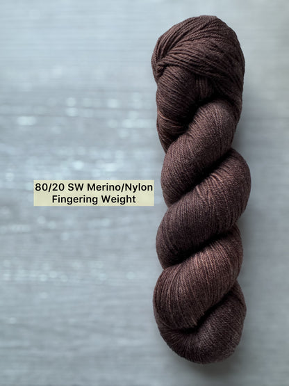 Brown skein of yarn on a gray background with text indicating yarn composition and weight.