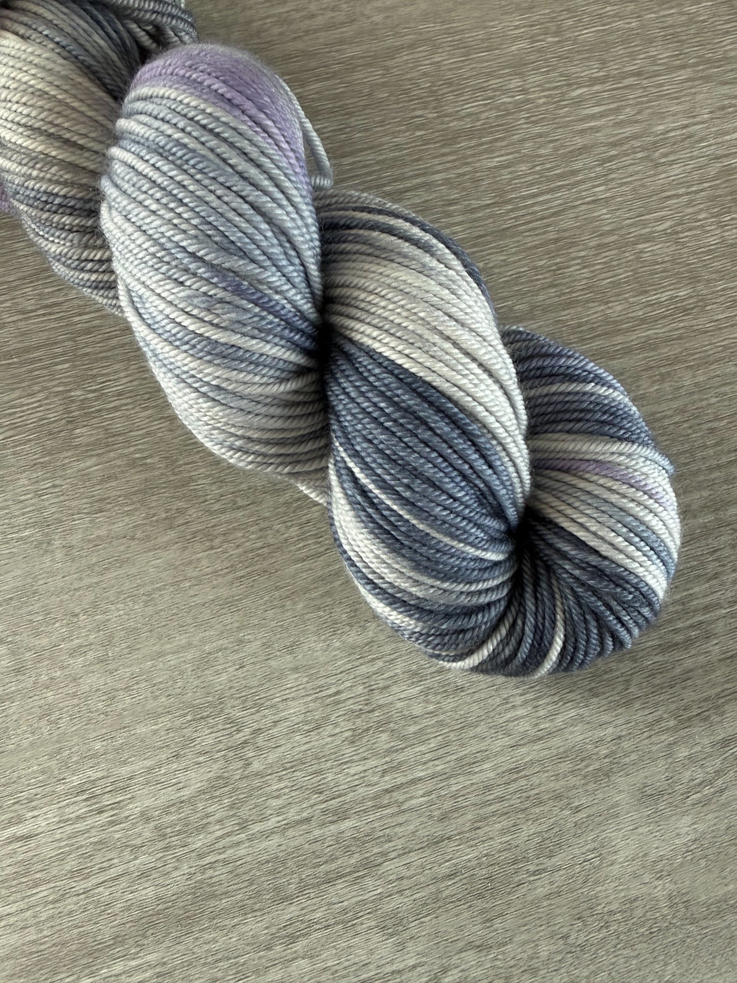 Hand-dyed ethically sourced merino wool yarn in deep blue, soft lilac, and muted gray, evoking twilight.