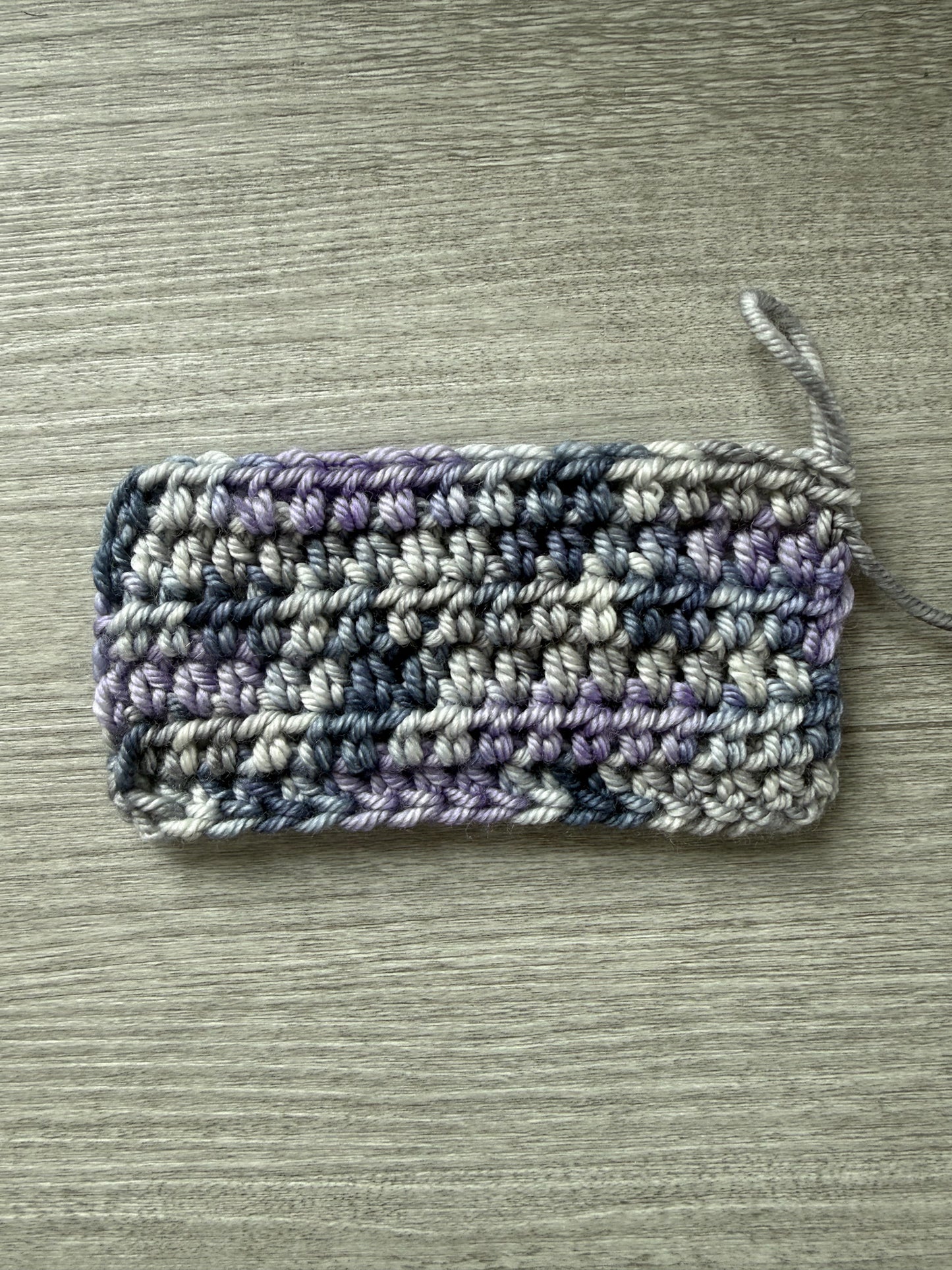 Crocheted swatch of ethically sourced merino wool yarn in deep blue, soft lilac, and muted gray.
