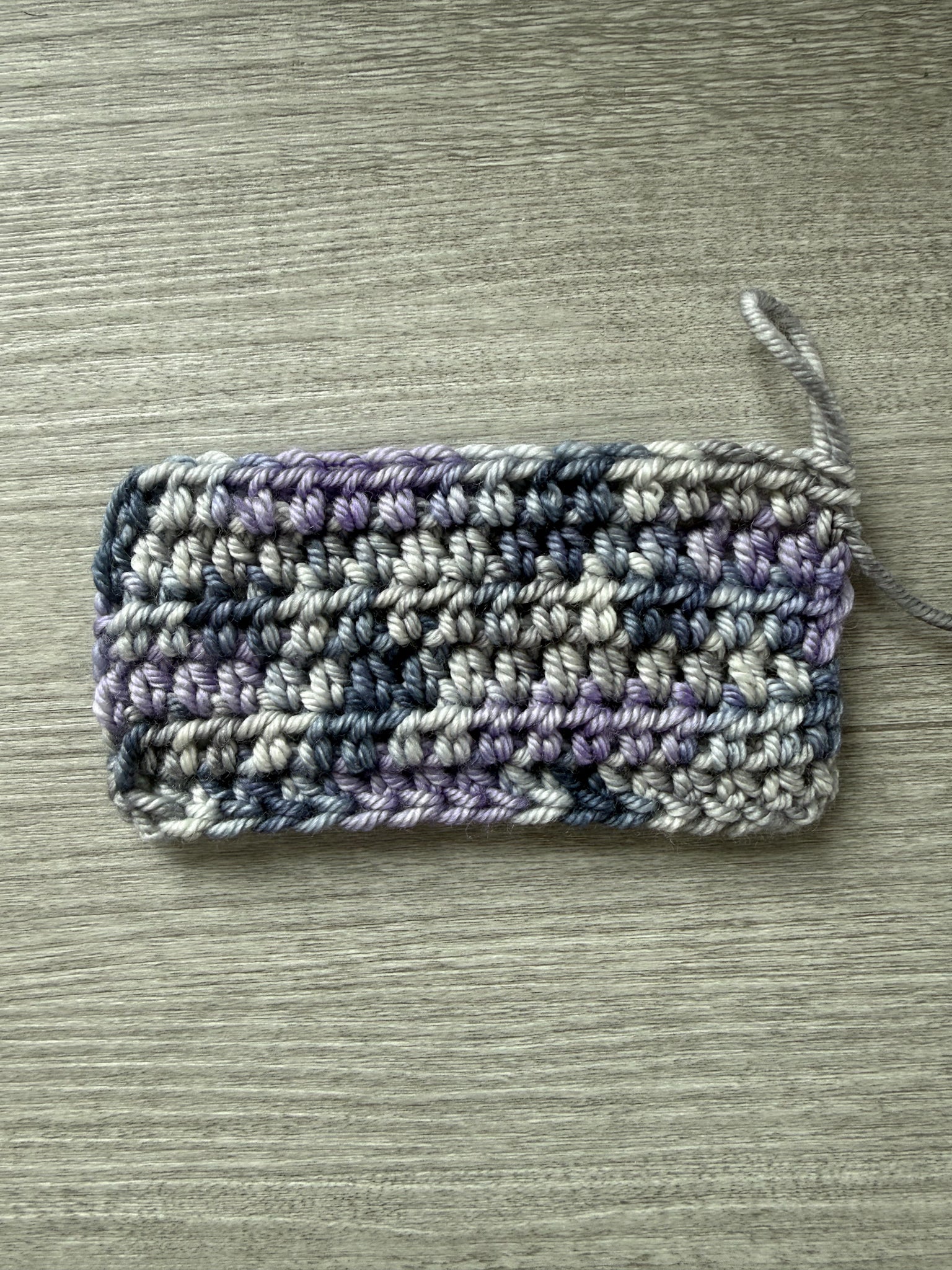 Crocheted swatch of ethically sourced merino wool yarn in deep blue, soft lilac, and muted gray.