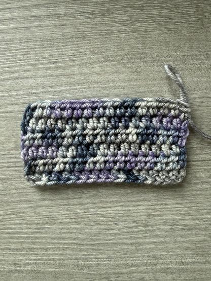 Crocheted swatch of ethically sourced merino wool yarn in deep blue, soft lilac, and muted gray.