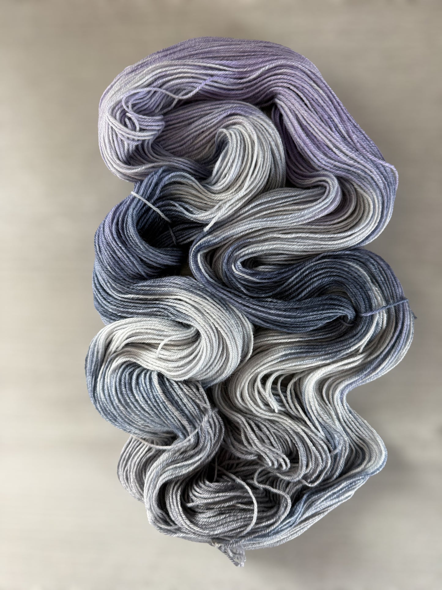 Hand-dyed ethically sourced merino wool yarn in deep blue, soft lilac, and muted gray, evoking twilight.