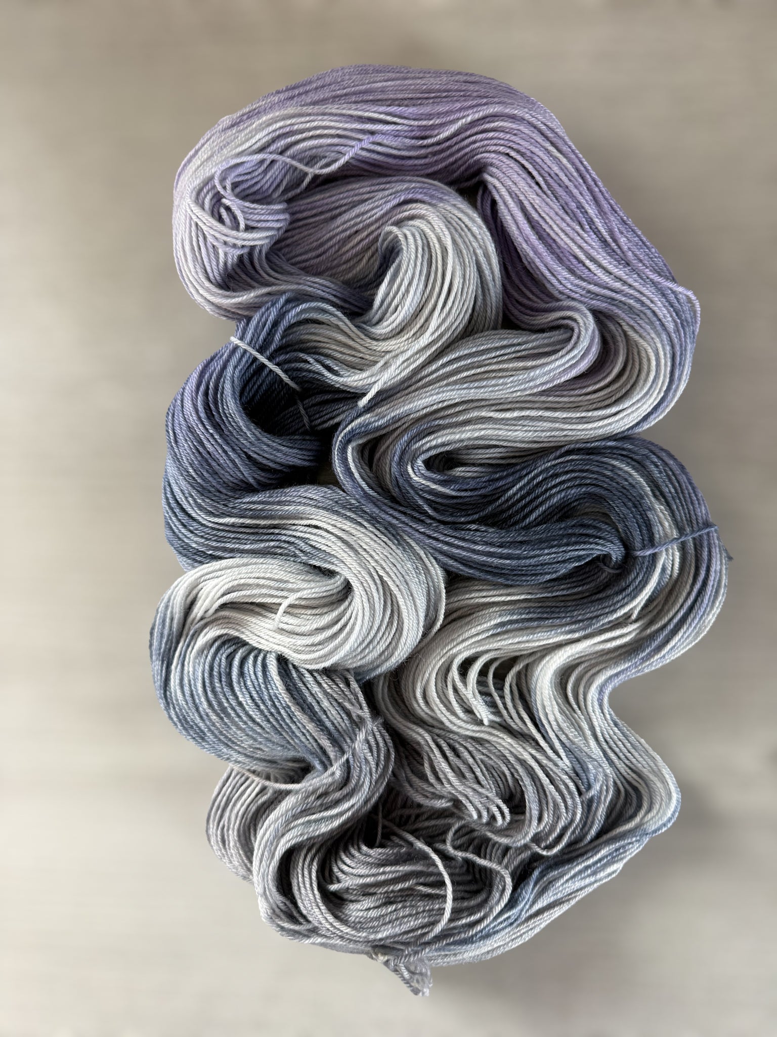 Hand-dyed ethically sourced merino wool yarn in deep blue, soft lilac, and muted gray, evoking twilight.