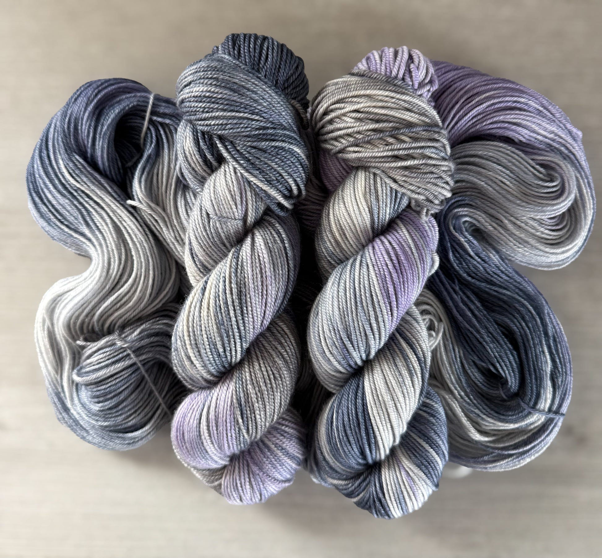 Hand-dyed ethically sourced merino wool yarn in deep blue, soft lilac, and muted gray, evoking twilight.