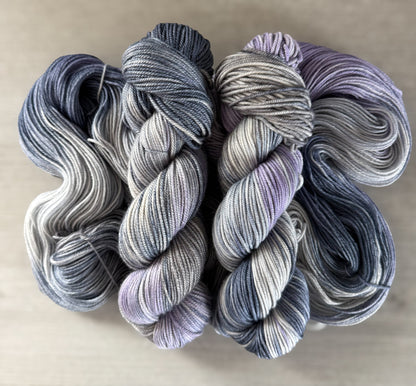 Hand-dyed ethically sourced merino wool yarn in deep blue, soft lilac, and muted gray, evoking twilight.