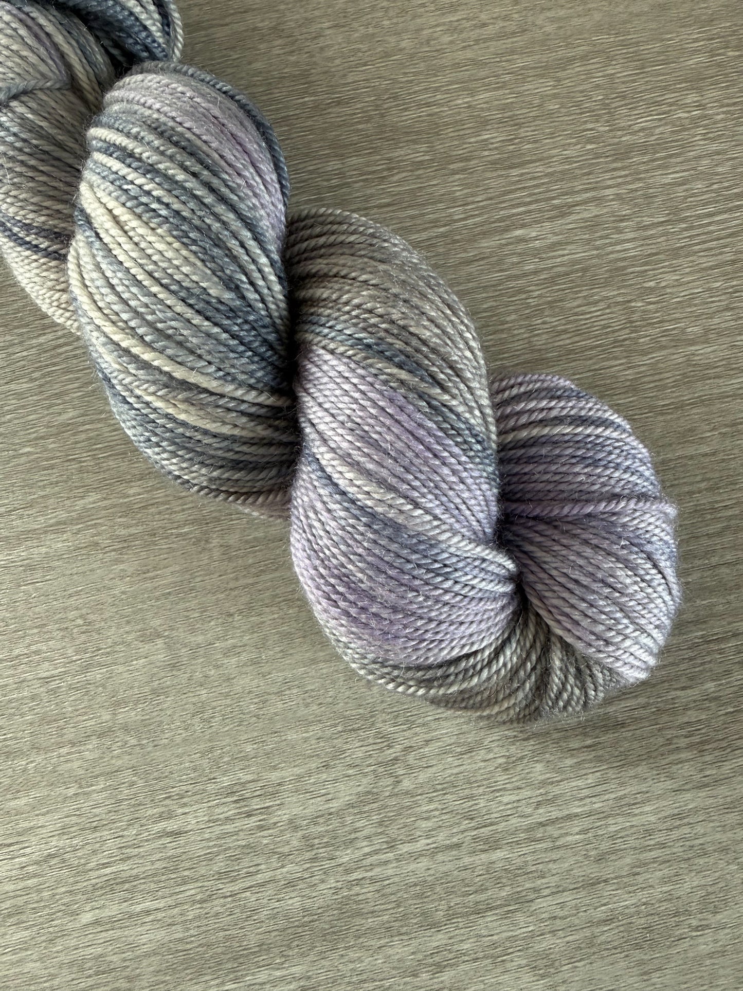 Hand-dyed ethically sourced merino wool yarn in deep blue, soft lilac, and muted gray, evoking twilight.