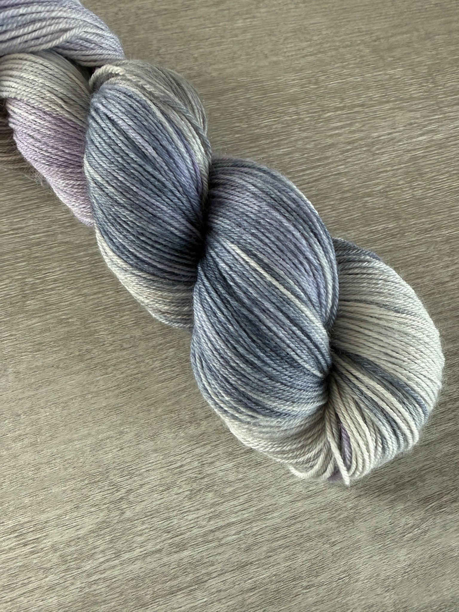 Hand-dyed ethically sourced merino wool yarn in twilight blues, lilacs, and grays, evoking a serene landscape.