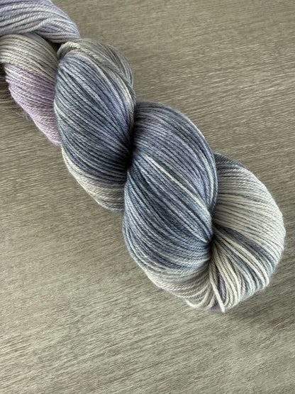 Hand-dyed ethically sourced merino wool yarn in twilight blues, lilacs, and grays, evoking a serene landscape.
