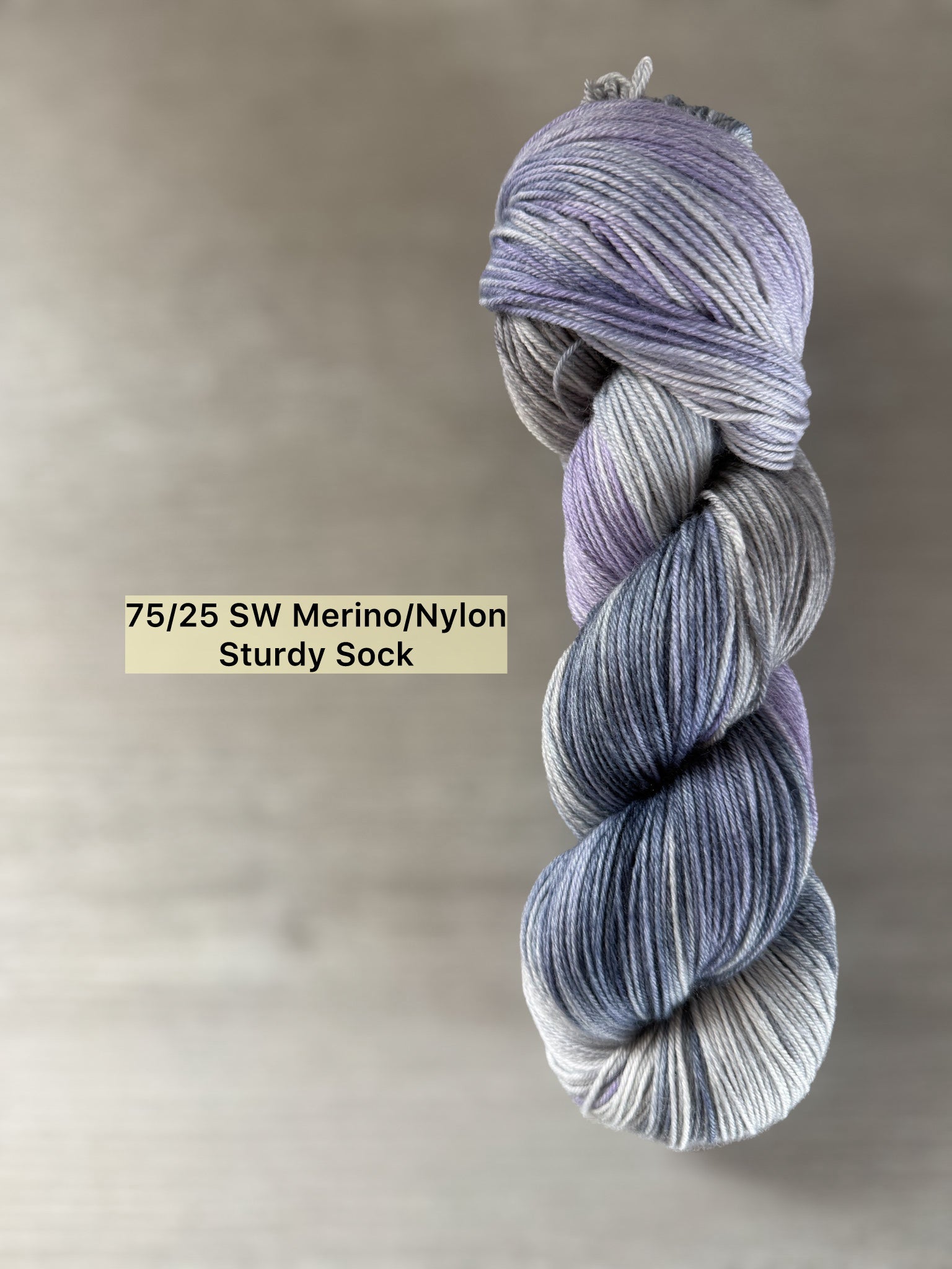 Hand-dyed "Echoes of Twilight" ethically sourced merino wool yarn in deep blue, lilac, and muted gray.
