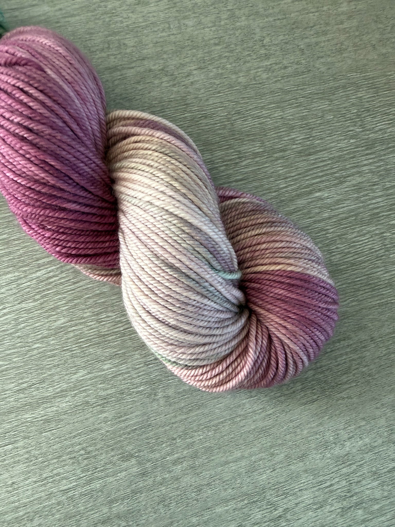 Ethically sourced merino wool yarn, hand-dyed in variegated plum, ivory, and sage green.