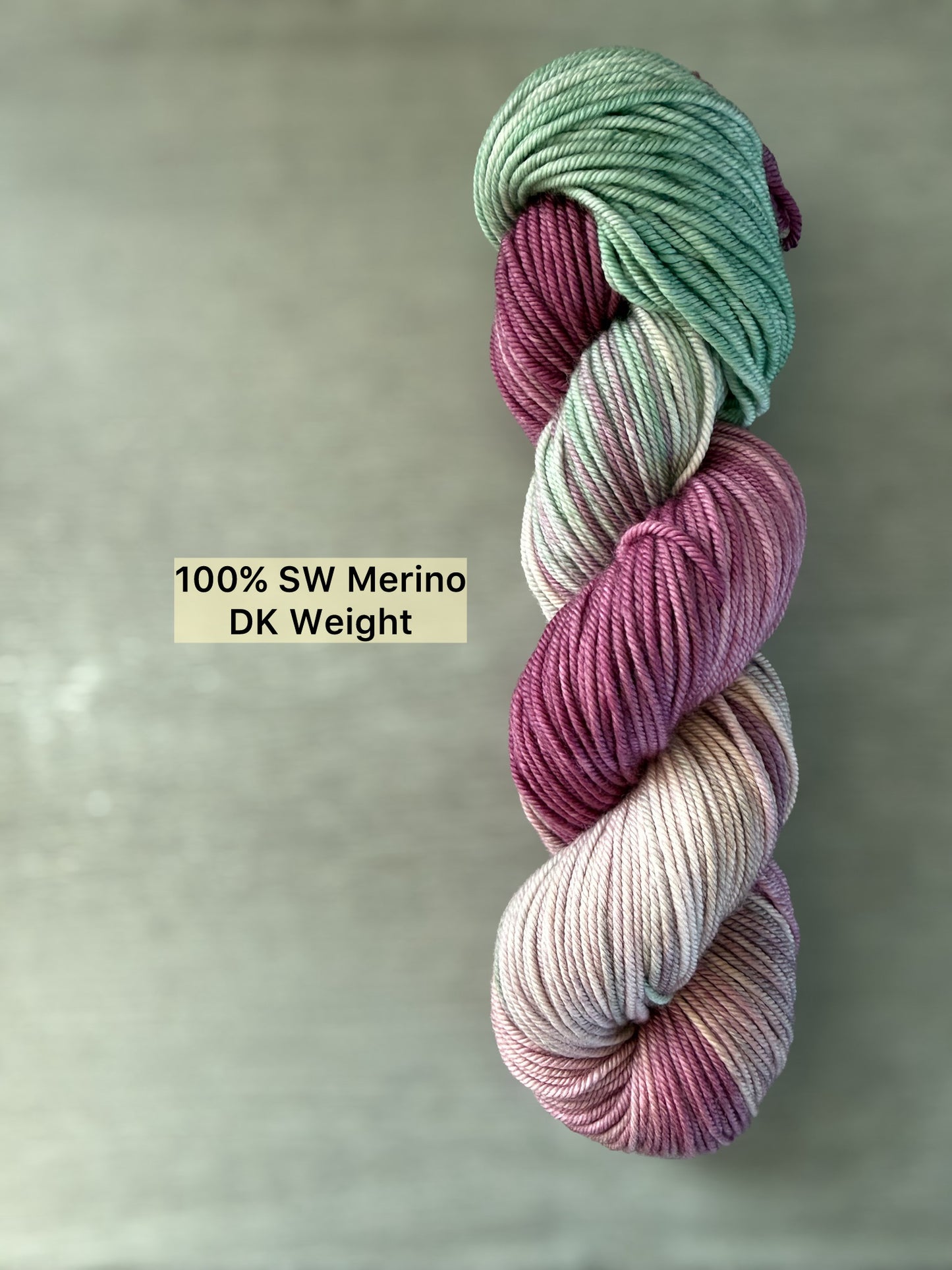 Ethically sourced DK weight merino wool yarn in plum, ivory, and sage green, hand-dyed with subtle transitions.