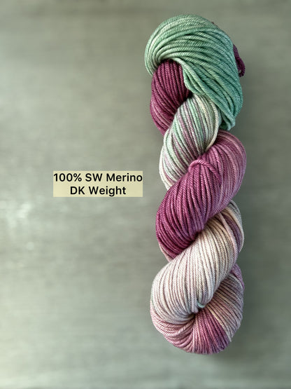 Ethically sourced DK weight merino wool yarn in plum, ivory, and sage green, hand-dyed with subtle transitions.