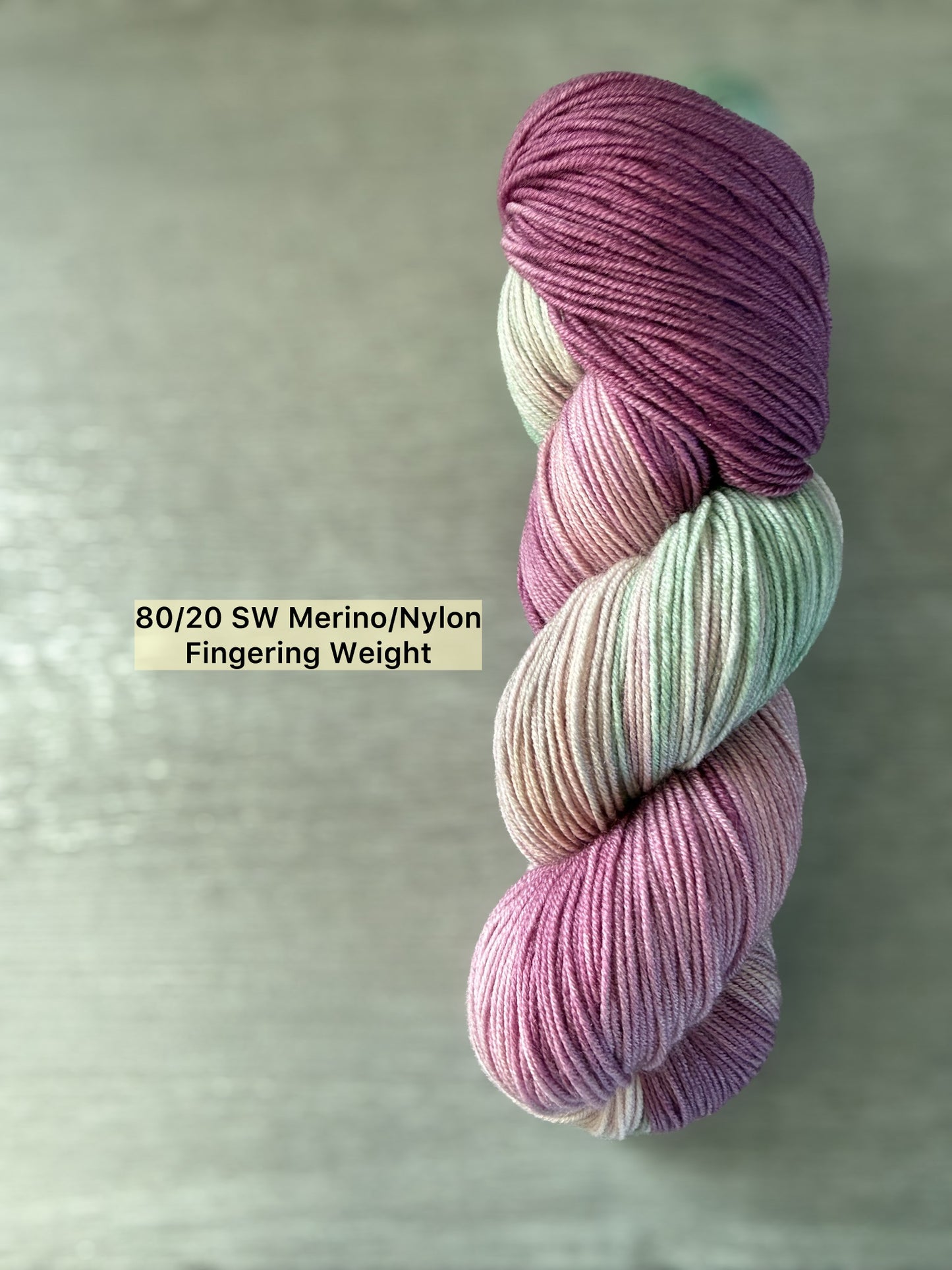 Hand-dyed Ethereal Meadows ethically sourced merino wool yarn in plum, ivory, and sage green.