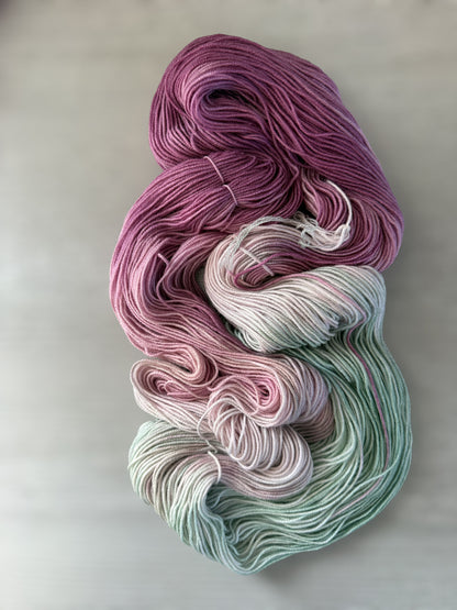 Hand-dyed ethically sourced merino wool yarn in variegated plum, ivory, and sage green.