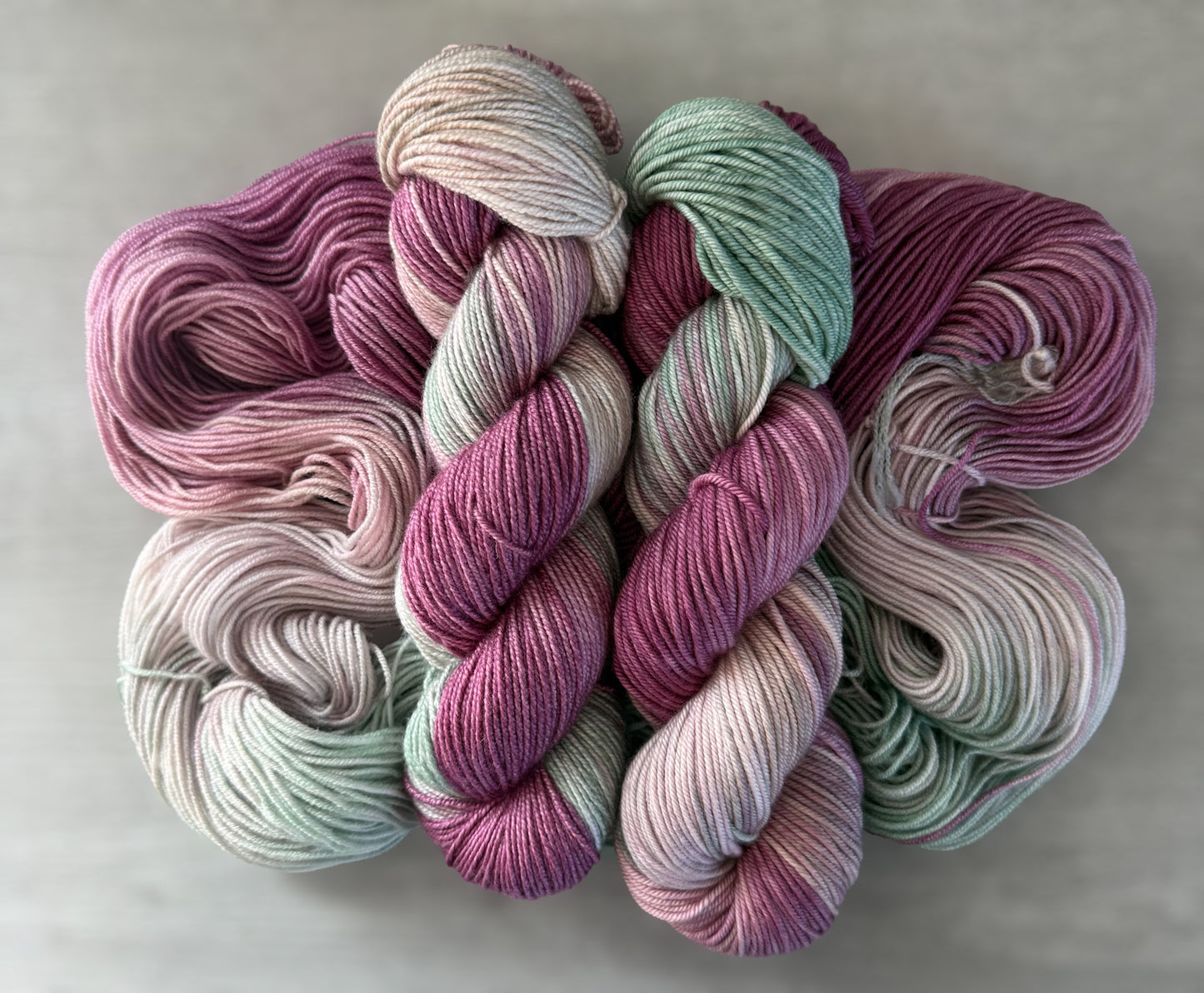 Ethically sourced merino wool yarn in plum, ivory, and sage green, hand-dyed with subtle watercolor transitions.