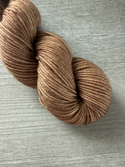 Ethically sourced "Lake House" hand-dyed merino wool yarn in soft and medium browns, displayed on wood.