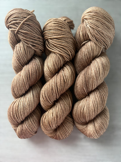Three skeins of "Lake House" hand-dyed ethically sourced merino wool yarn in soft and medium browns.