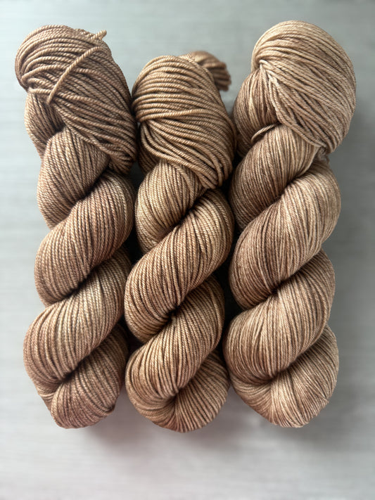 Three skeins of "Lake House" hand-dyed ethically sourced merino wool yarn in soft and medium browns.