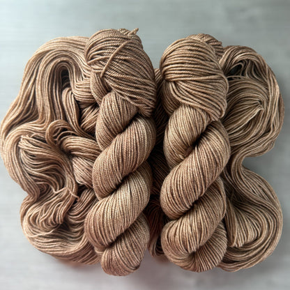 Two skeins of "Lake House" hand-dyed ethically sourced merino wool yarn in soft and medium browns.