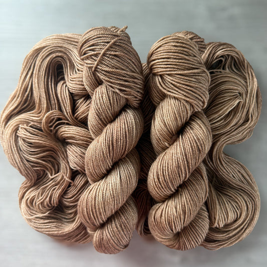 Two skeins of "Lake House" hand-dyed ethically sourced merino wool yarn in soft and medium browns.