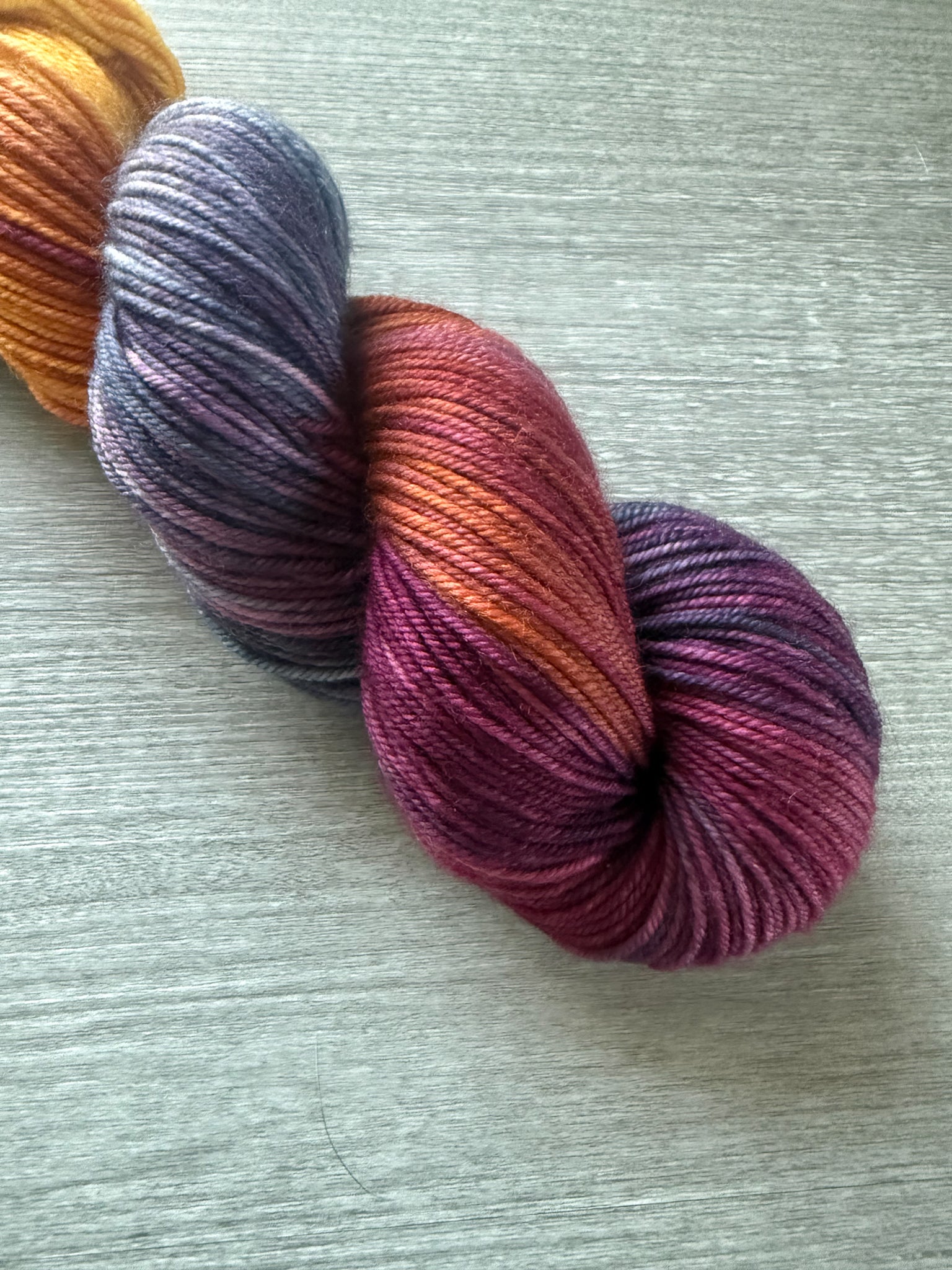 Ethically sourced Malabar Squirrel hand-dyed merino wool yarn with variegated blues, golden yellow, and burgundy.