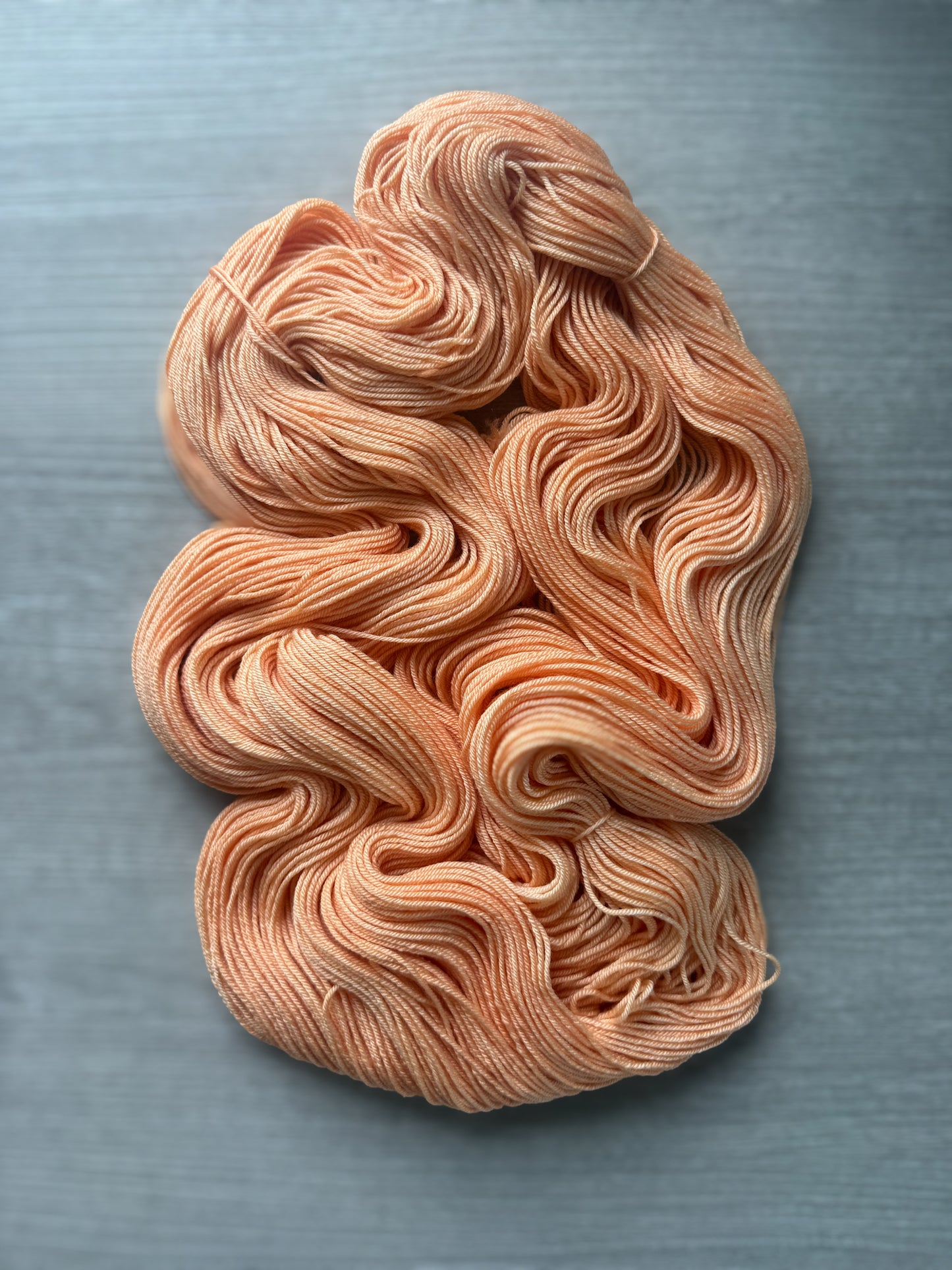 Ethically sourced "Melon Dollar Smile" hand-dyed merino wool yarn in a vibrant coral-peach hue.