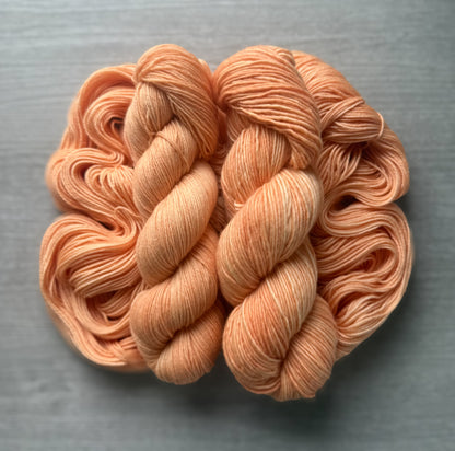 Two skeins of "Melon Dollar Smile" hand-dyed, ethically sourced merino wool yarn in vibrant coral-peach.