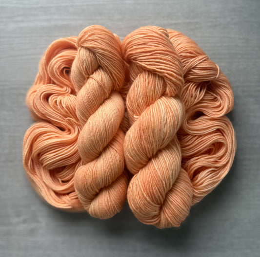 Two skeins of "Melon Dollar Smile" hand-dyed, ethically sourced merino wool yarn in vibrant coral-peach.
