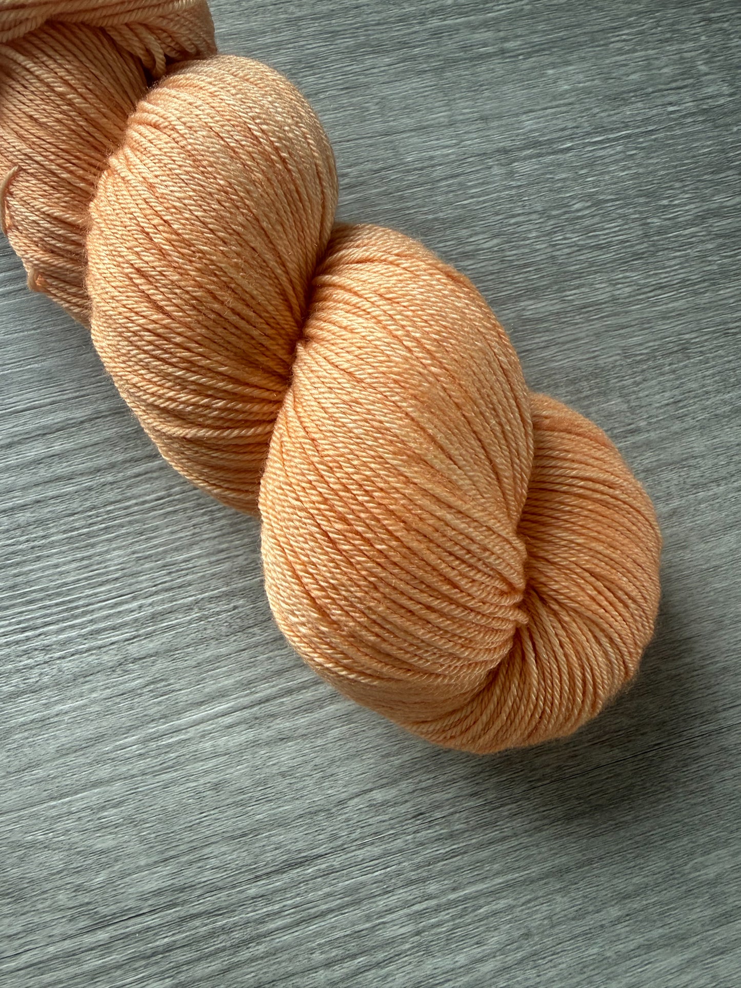 Skein of Melon Dollar Smile ethically sourced hand-dyed merino wool yarn in a vibrant coral-peach hue.