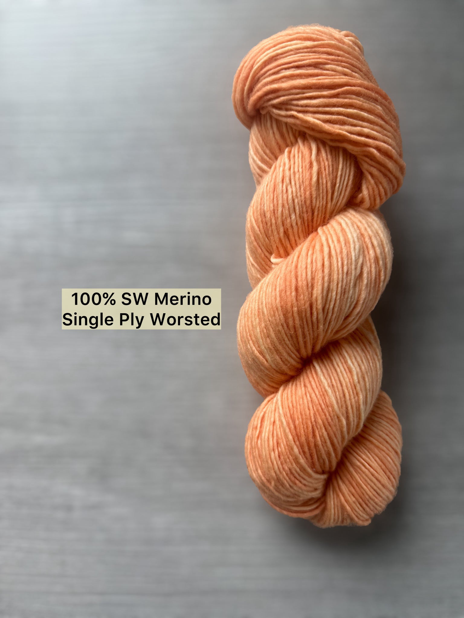 Skein of "Melon Dollar Smile" hand-dyed, ethically sourced, super soft merino wool yarn in a vibrant coral-peach hue.