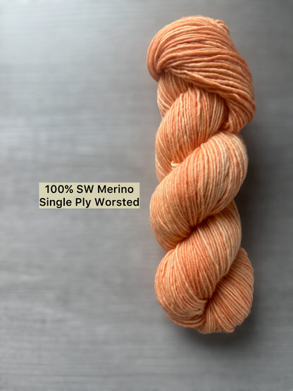 Skein of "Melon Dollar Smile" hand-dyed, ethically sourced, super soft merino wool yarn in a vibrant coral-peach hue.