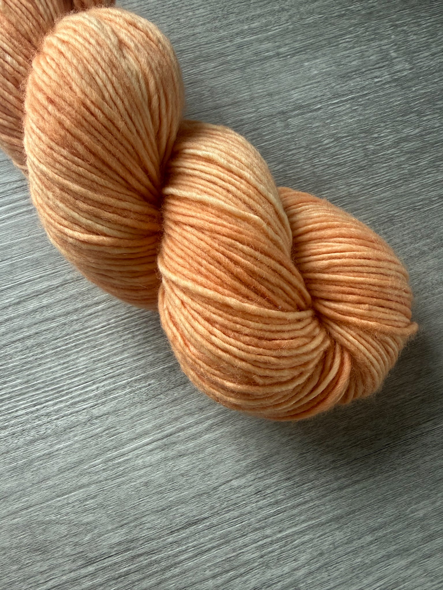 Ethically sourced "Melon Dollar Smile" hand-dyed merino wool yarn in a vibrant coral-peach hue.