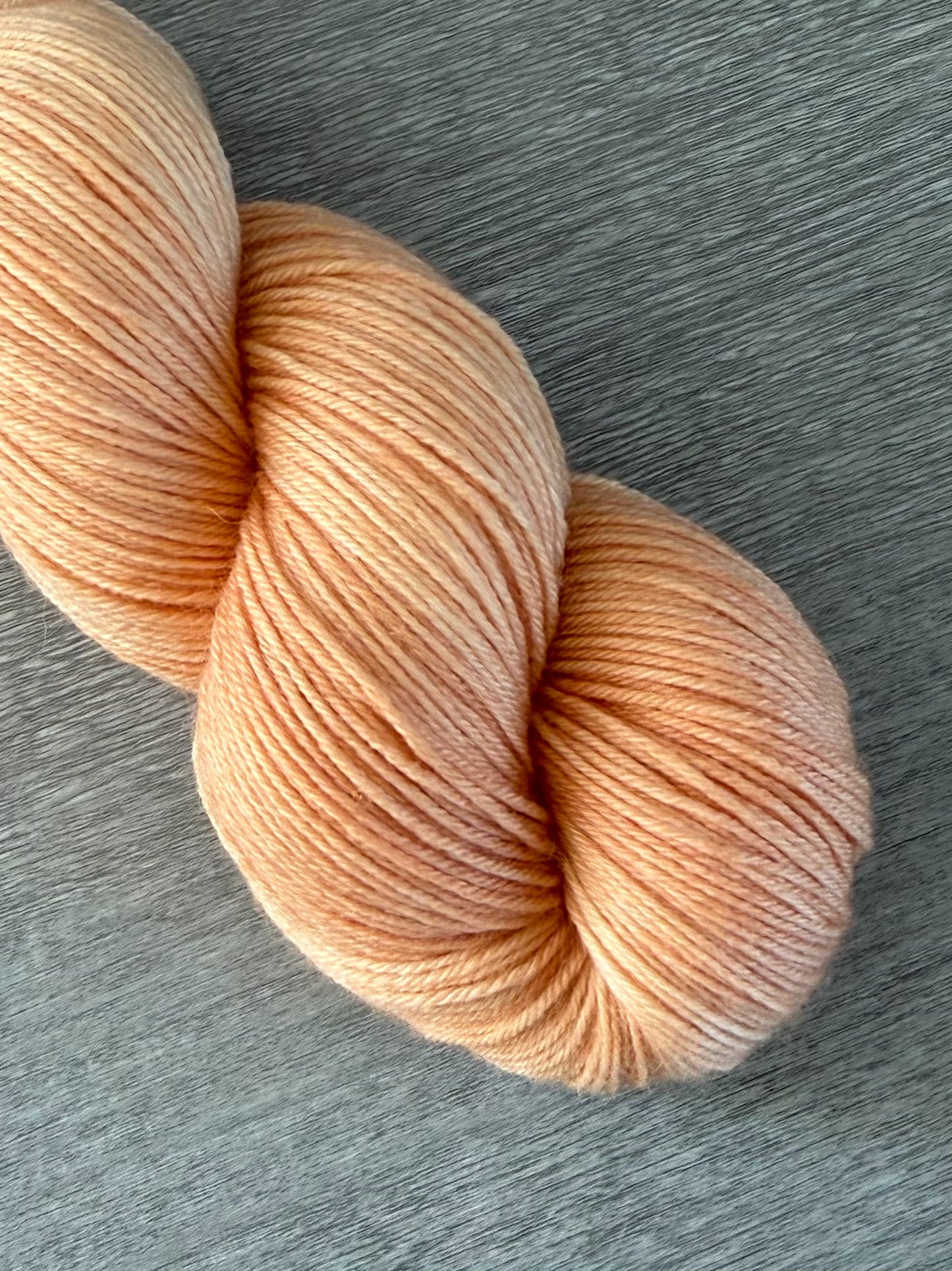 Skein of ethically sourced "Melon Dollar Smile" hand-dyed merino wool yarn in vibrant coral and peach tones.
