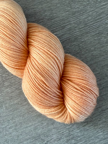 Skein of ethically sourced "Melon Dollar Smile" hand-dyed merino wool yarn in vibrant coral and peach tones.