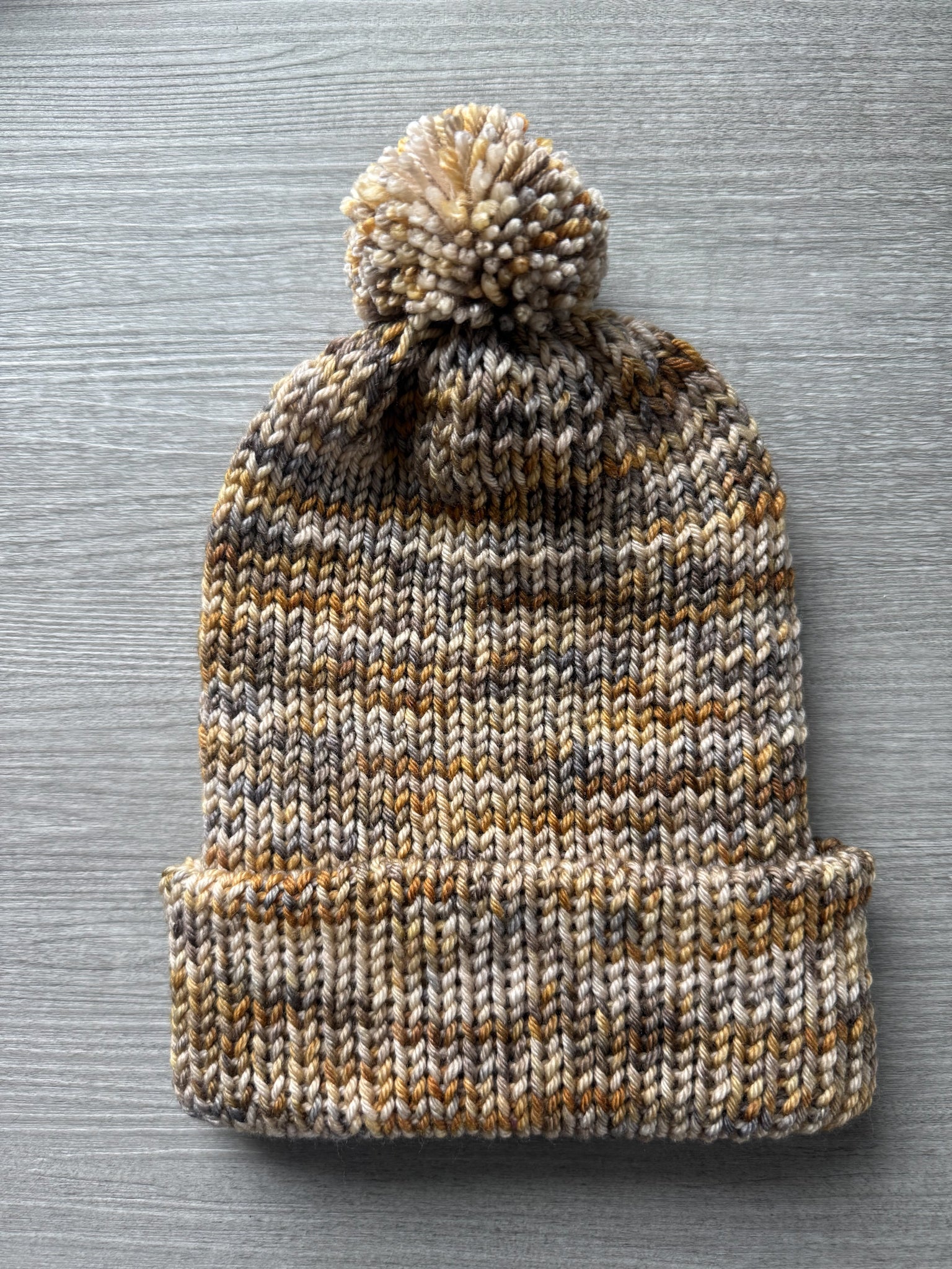 Hand-knitted beanie from Mesa Artisan ethically sourced merino wool yarn, featuring beige, charcoal, taupe, and ocher.